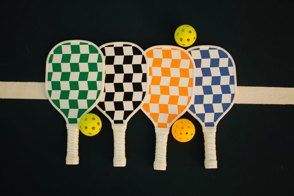 Four checkerboard-patterned pickleball paddles with wiffle balls on a sports court.